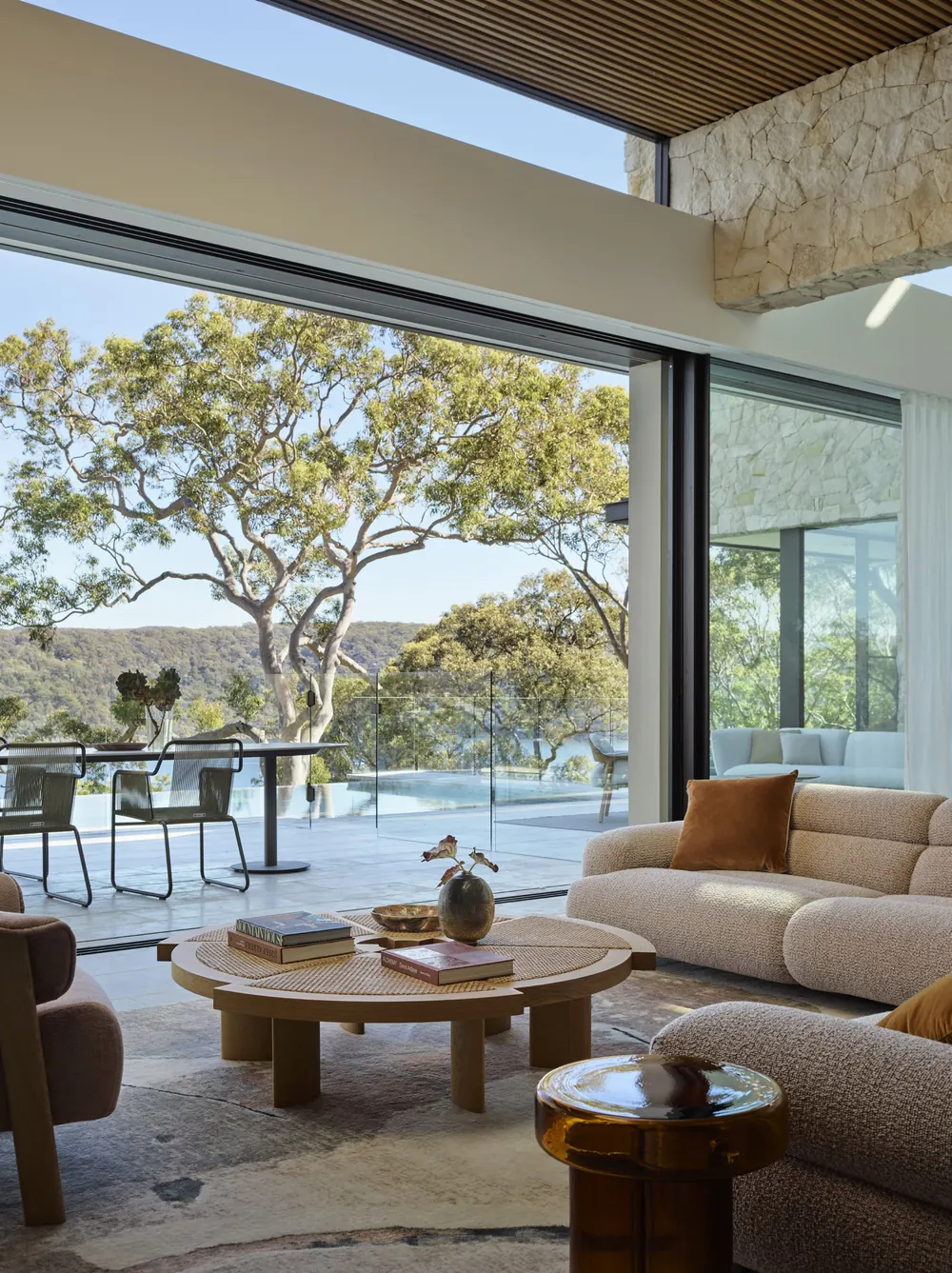 Living room opening to a terrace and pool with treetop views